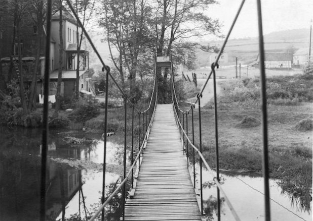 1928 wurde die Hängebrücke als „Bismarck-Steg“ gebaut. Das historische Foto zeigt die Hängebrücke über die Wisser im Jahr der Fertigstellung mit der „Villa“ (links) und den Häusern „Auf der Au“ (hinten rechts) - Foto: Archiv/H.-J. Schuh.