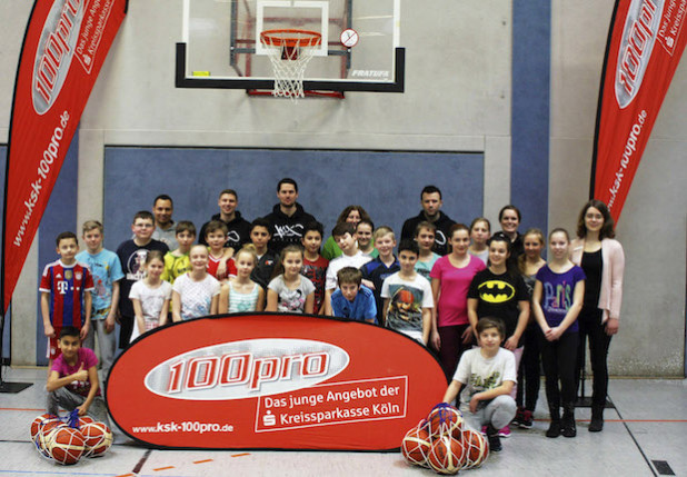 Annika Stiebig , 100pro - Jugendbetreuerin der Kreissparkasse Köln in Waldbröl (rechts), begrüßte Schülerinnen und Schüler der Gesamtschule Waldbröl zum 100pro-Basketball Training mit Matthias Sonnenschein, Savo Milovic und Sascha Tretnjak vom ProA-Ligisten Dragons Rhöndorf (Quelle: Kreissparkasse Köln)