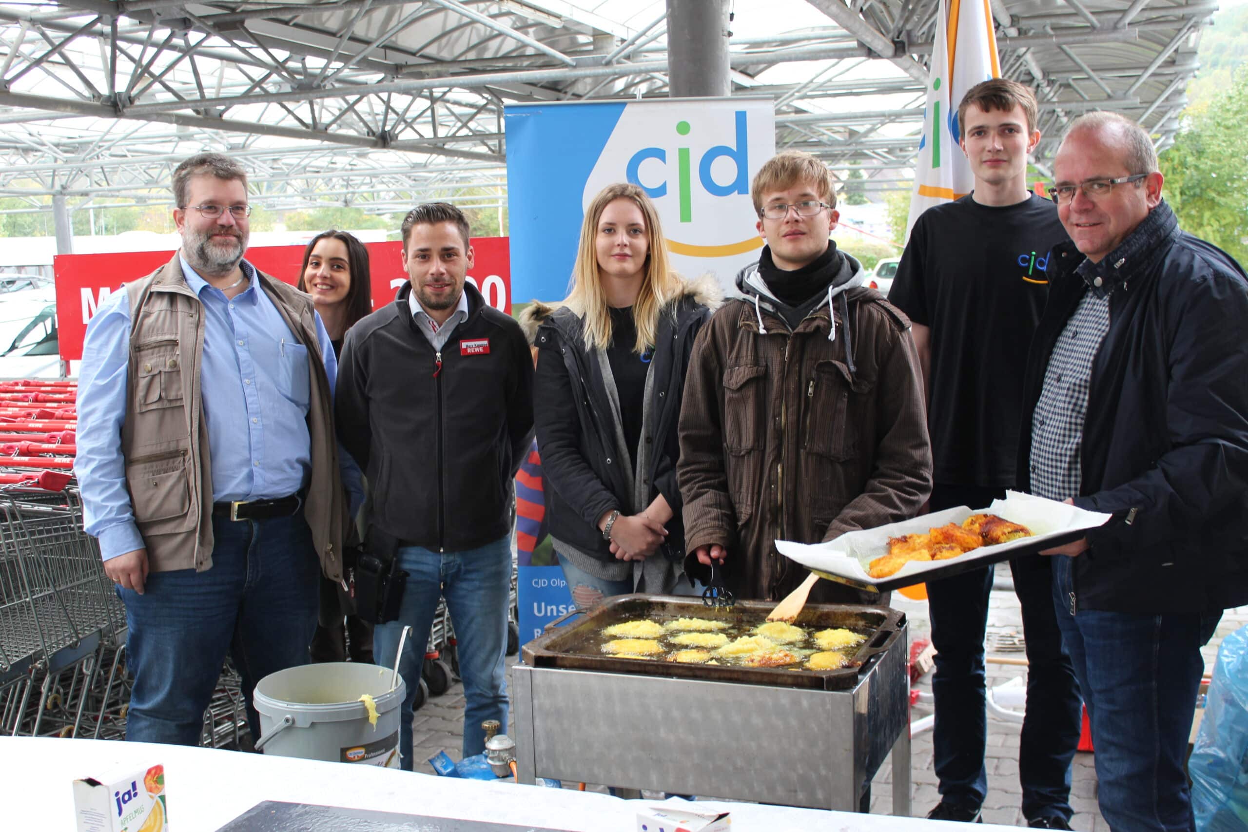 Foto: CJD Ausbilder Stefan Borner (links), REWE Marktleiter Kai Knappe (3. v.l.), CJD Einrichtungsleiter Markus Bröcher (rechts) zusammen mit den Jugendlichen bei der Reibekuchenzubereitung.